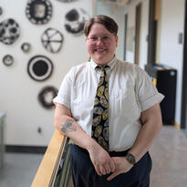Photo of Maddy, a white nonbinary person with a short brown hair, smiling and wearing a white button-up and floral tie.